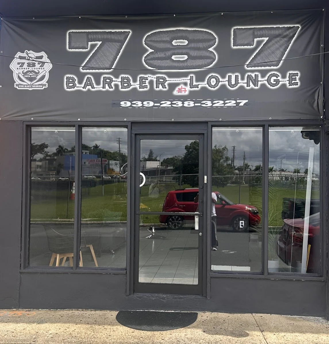 Fachada de 787 Barber Lounge en Bayamón: local gris con rótulo 787 Barber Lounge, escudo con tijera y navajas, y el teléfono 939-238-3227