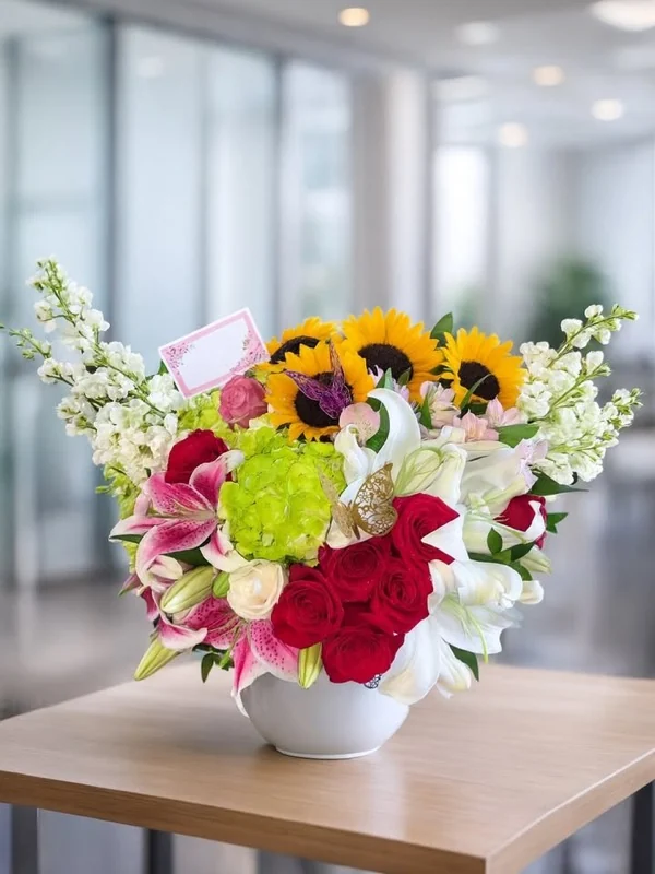 Arreglo mixto de girasoles, lirios rosados, rosas rojas y hortensia verde en base blanca