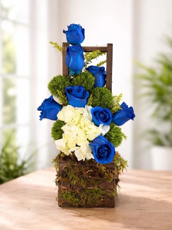 Arreglo de rosas azules con hortensia blanca sobre base de madera y musgo