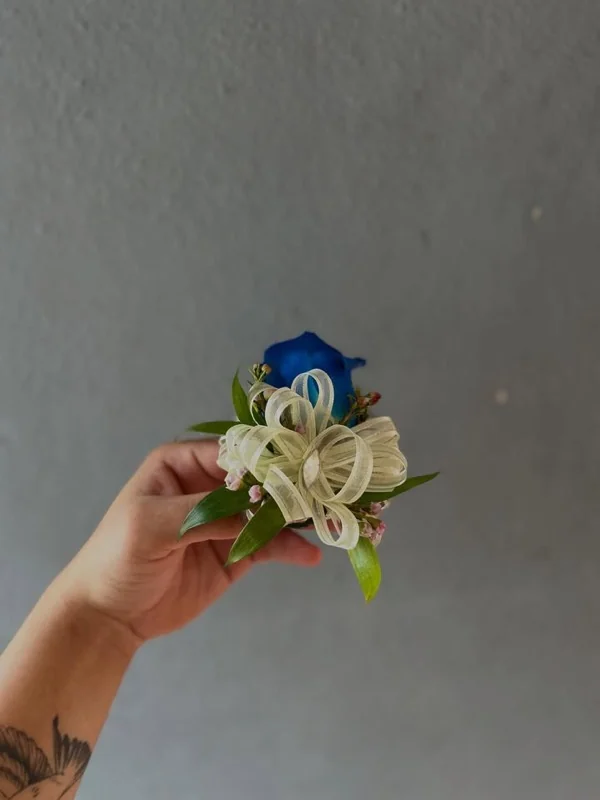 Boutonniere de rosa azul con lazo blanco en la mano de nuestra florista