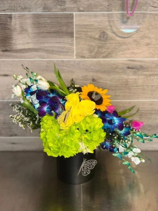 Arreglo de orquídeas azules, girasol y hortensia verde en caja negra