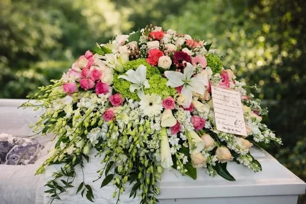 Manto floral de rosas y lirios sobre féretro blanco al aire libre, hecho por Alvit