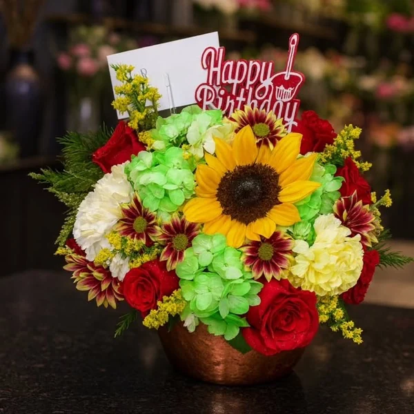 Arreglo de cumpleaños con girasol, rosas rojas y hortensias sobre el mostrador de Alvit