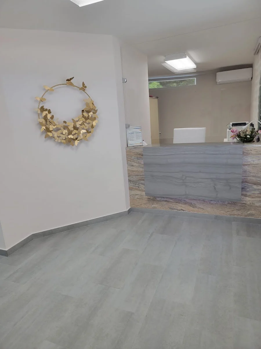 Recepción de Desalden Clinic con corona de mariposas doradas en la pared y mostrador de mármol