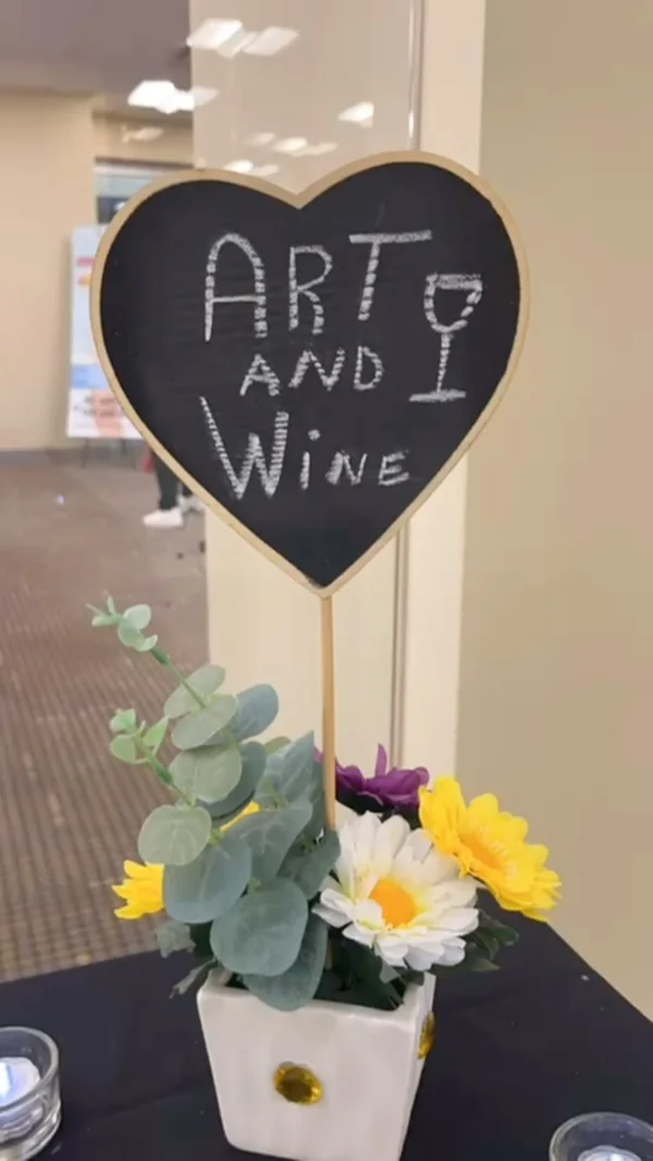 Letrero de pizarra en forma de corazón que lee Art and Wine, junto a flores