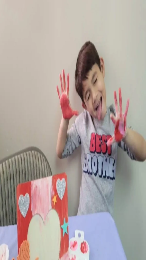 Niño sonriendo con las palmas de las manos cubiertas de pintura roja