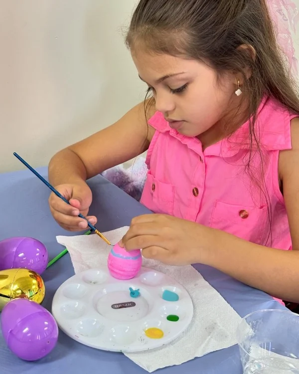 Niña concentrada pintando con un pincel delgado sobre su proyecto