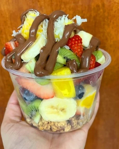Bowl de fruta con granola y sirop de chocolate sostenido en la mano