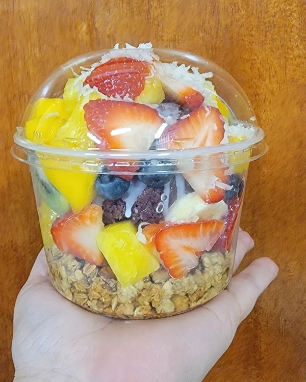 Bowl con fresa, mango, blueberries, granola y coco rallado sostenido en la mano