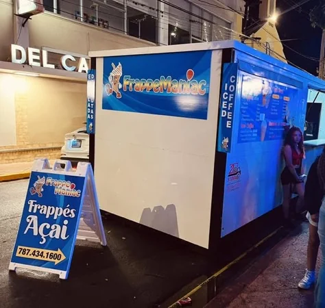 Kiosco azul de FrappeManiac de noche en Cidra con el rótulo de Frappés y Açaí en la acera