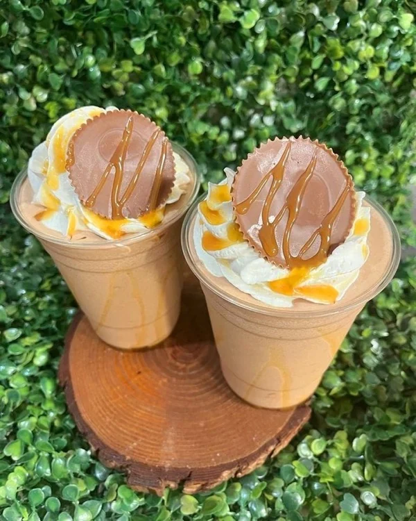 Dos frappés de chocolate con una taza de crema de maní encima y sirop de caramelo