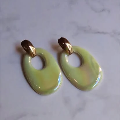 Pantallas ovaladas nacaradas en tono verde suave con broche dorado sobre mármol