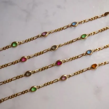 Cuatro cadenas doradas tipo figaro con gemas ovaladas multicolor sobre mármol