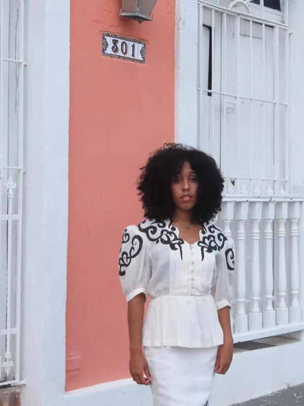 Conjunto vintage blanco con bordado negro frente a una fachada coral del Viejo San Juan