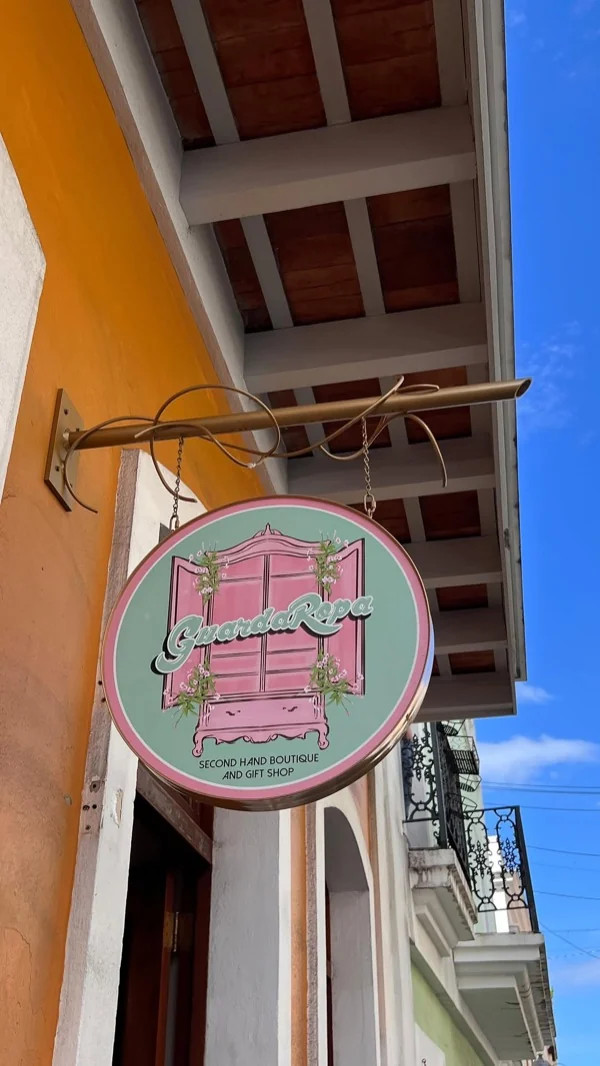 Letrero circular de GuardaRopa con armario rosado colgando de un balcón colonial contra el cielo azul
