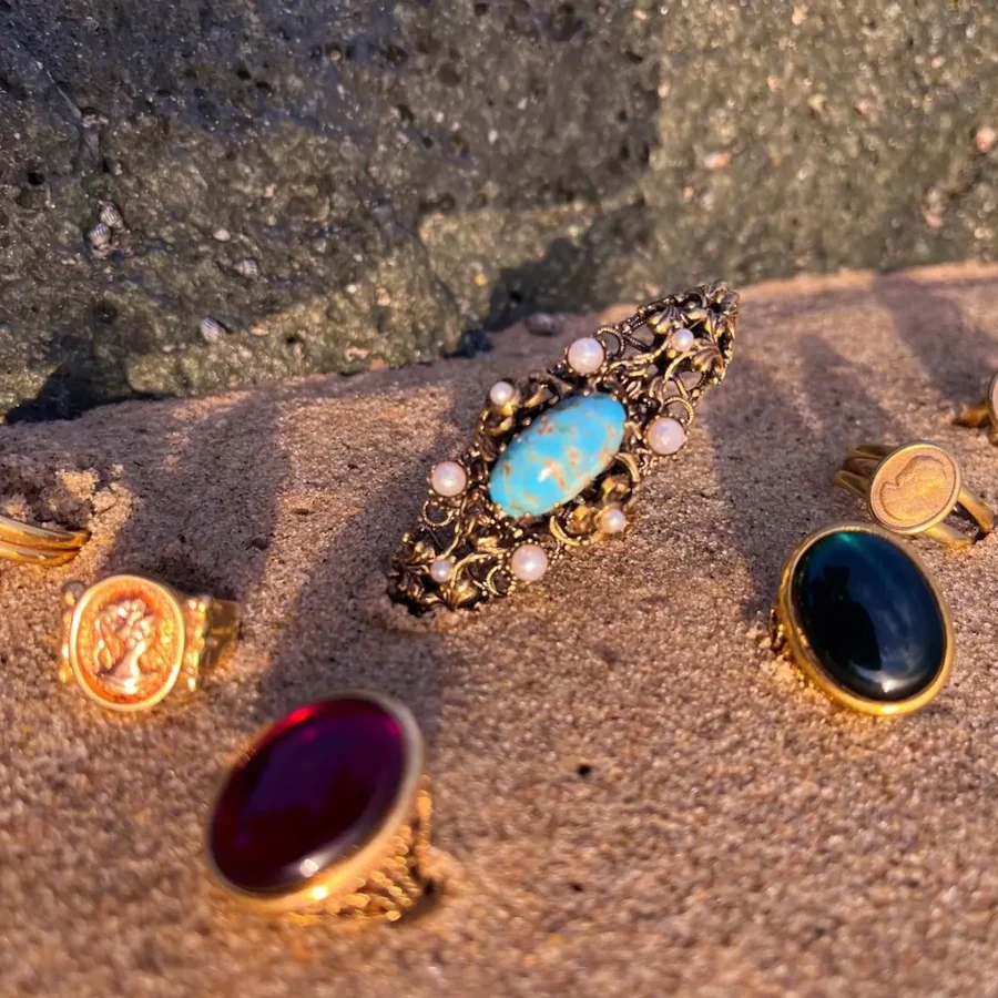 Sortijas vintage con turquesa, perlas y gemas de colores sobre arena dorada al atardecer