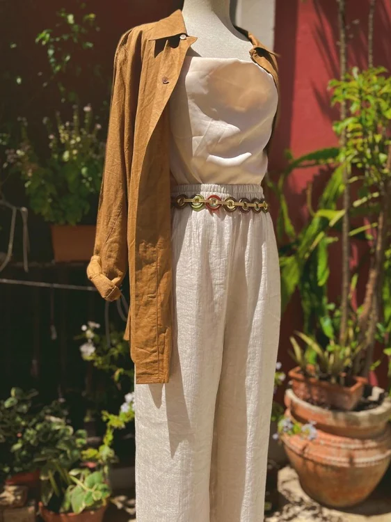Conjunto de lino natural con chaqueta camel y correa de eslabones dorados en un patio con plantas