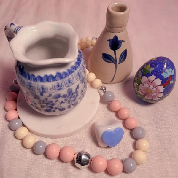 Jarrita de porcelana azul, huevo cloisonné y collar de perlas pastel sobre tela rosada