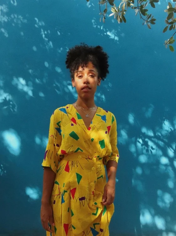 Vestido amarillo con estampado geométrico noventoso contra una pared azul con sombras de árbol