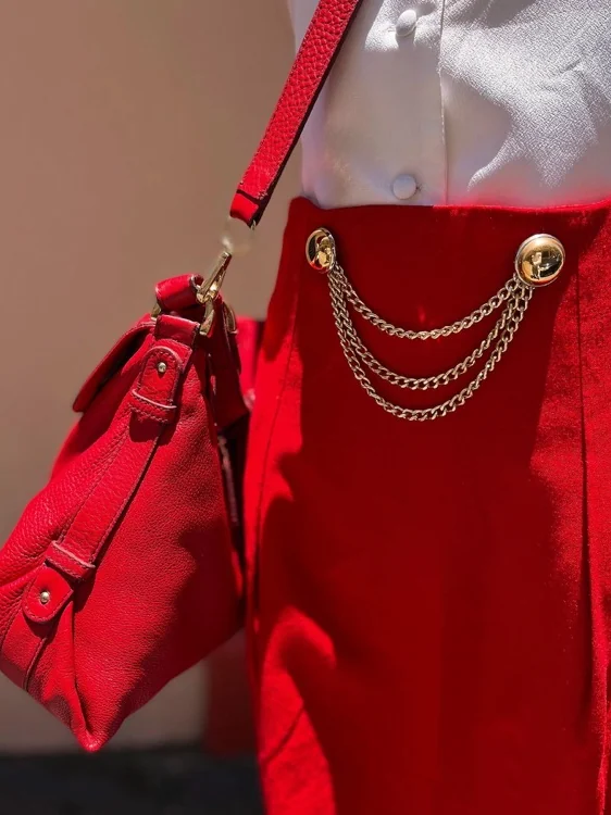 Falda roja con botones dorados y cadenas, con cartera de piel roja al hombro