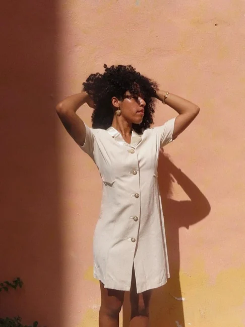 Vestido camisero crema con botones frente a una pared rosada al atardecer