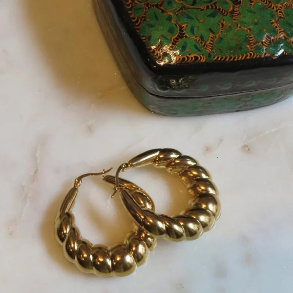 Aros dorados estilo croissant sobre mármol junto a una caja decorativa verde