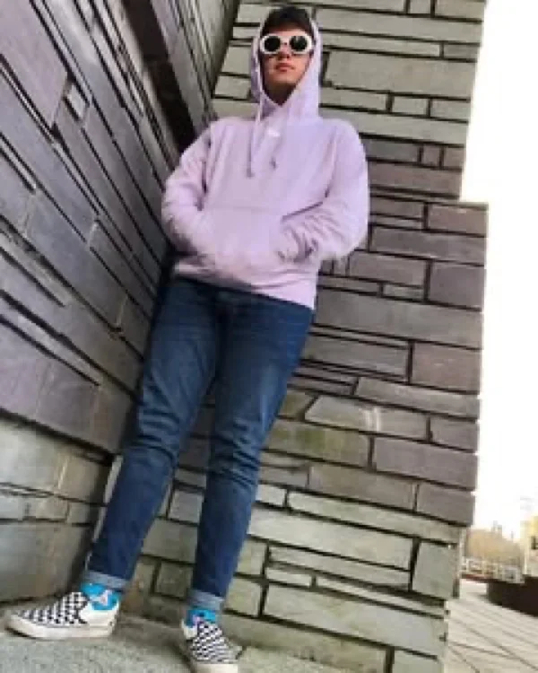 Hoodie JUNZI lila con capucha puesta, recostado de una pared de ladrillo