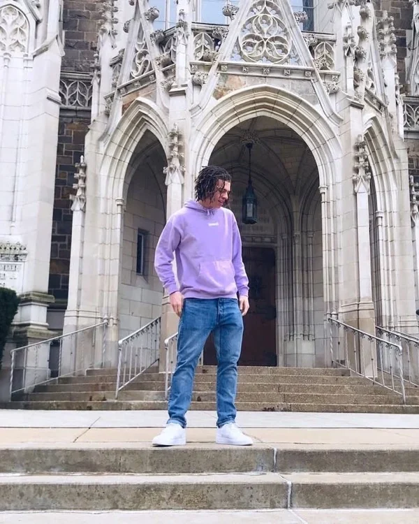 Persona con hoodie JUNZI lila en las escalinatas de un edificio gótico
