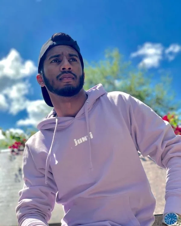 Persona con hoodie JUNZI lila y gorra al revés bajo un cielo azul