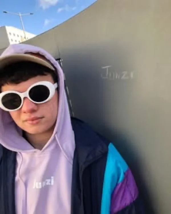 Persona con la capucha lila puesta junto a una pared donde alguien escribió Junzi