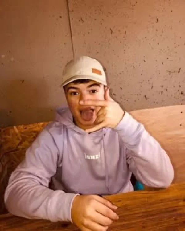 Persona con hoodie JUNZI lila y gorra, sentada en una mesa de madera