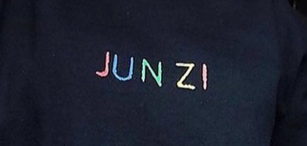 Macro del bordado JUNZI sobre tela oscura, cada letra en un hilo de color distinto