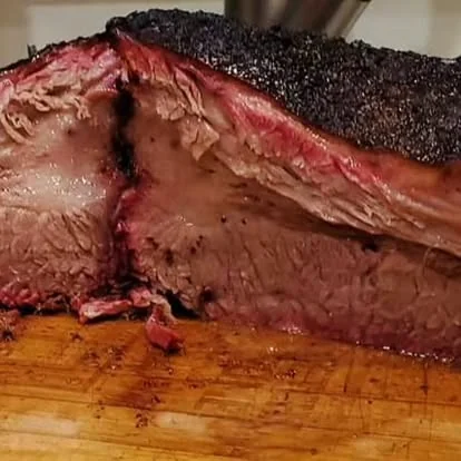 Brisket entero recién cortado mostrando el smoke ring sobre tabla de madera