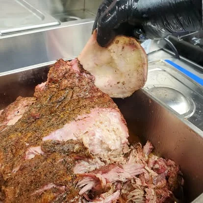 Pork butt ahumado siendo desmenuzado a mano con guantes negros