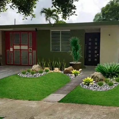 Front-yard xeriscaping con agaves, piedra y boulders frente a residencia verde en PR