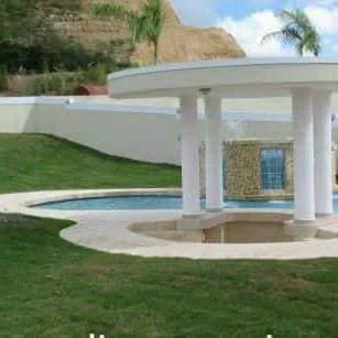 Área de piscina con gazebo de columnas blancas y grama en pendiente en Puerto Rico