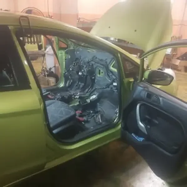 Ford Fiesta verde con el capó abierto y el interior desmontado en el taller