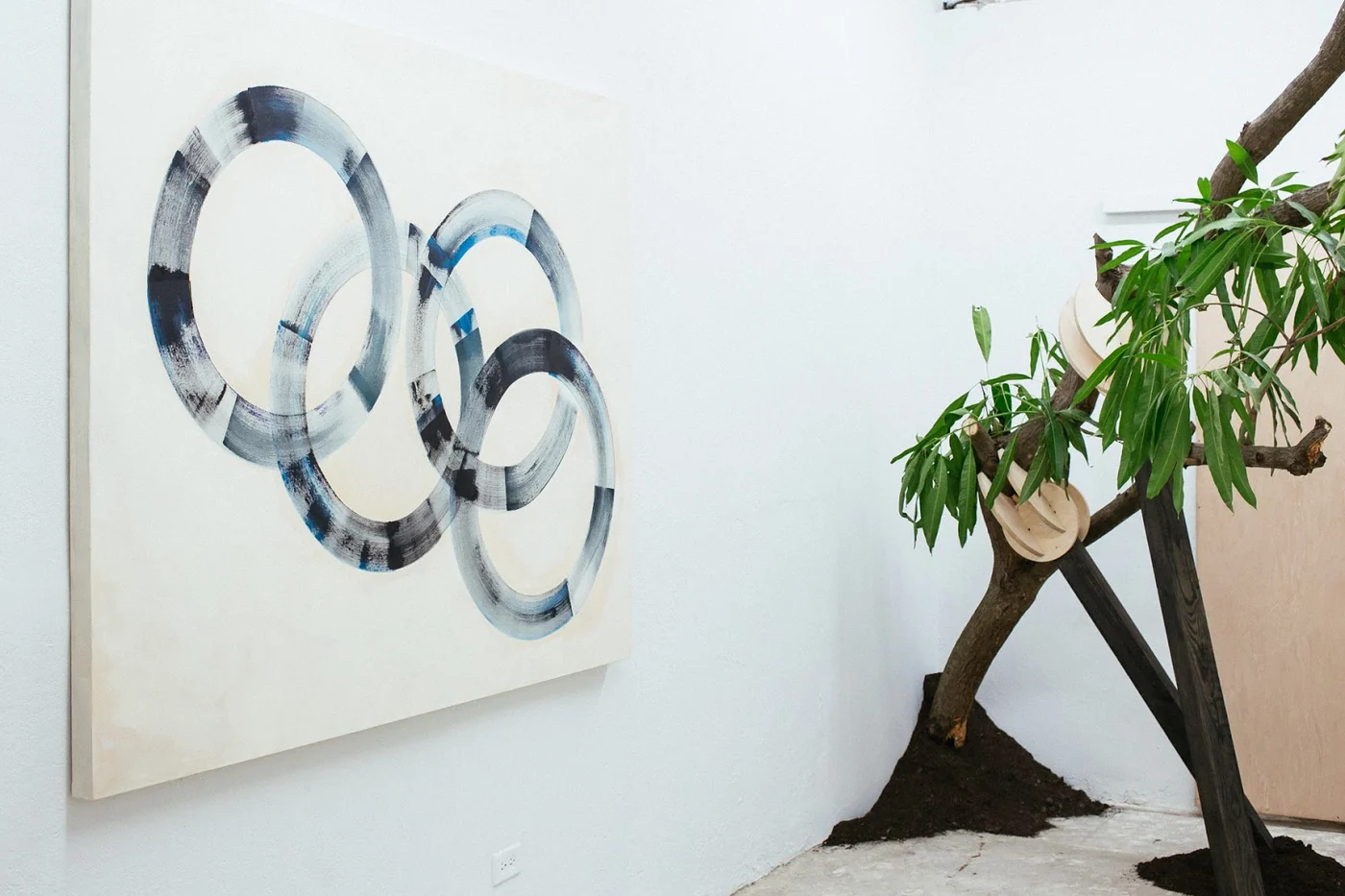 Pintura abstracta de aros entrelazados junto a escultura de rama y tierra en Recinto Cerra