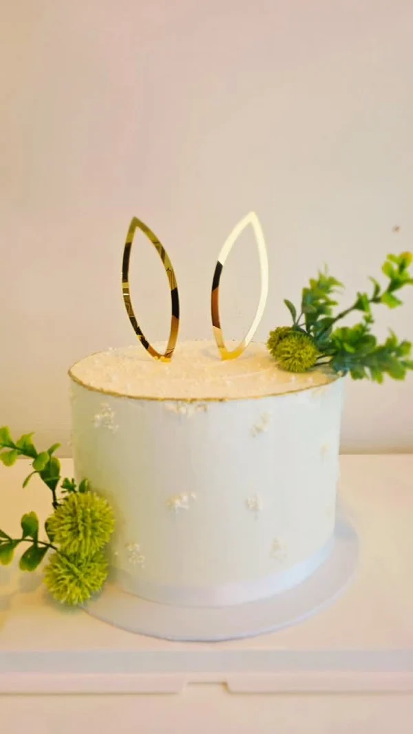 Cake blanco con topper dorado de orejas de conejo y follaje