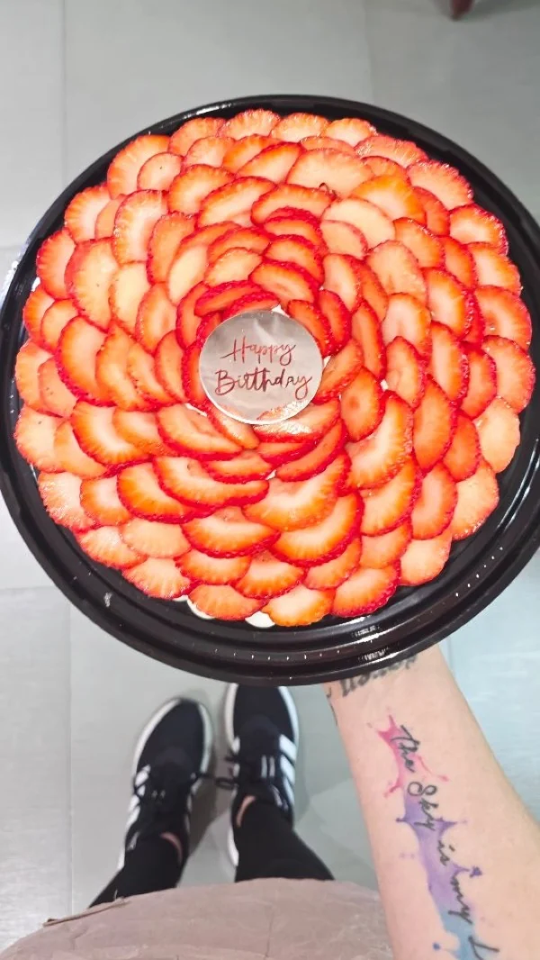 Tarta de fresas en flor sostenida en mano, con el tatuaje The Sky is my Limit visible