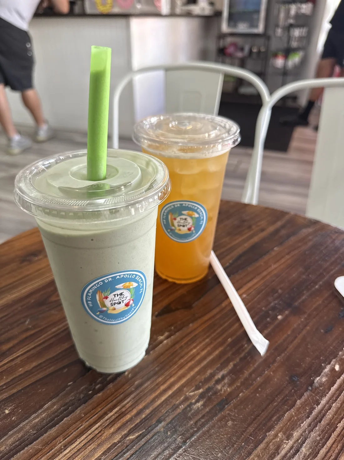 Smoothie verde con sorbeto ancho junto a un tea anaranjado sobre la mesa de madera del local