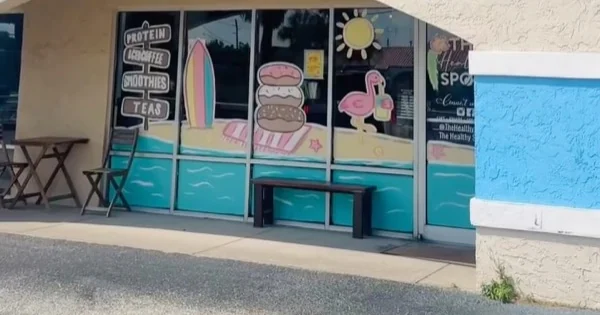 Fachada del local con la ventana pintada a mano: protein, coffee, smoothies y teas, con tabla de surf y flamenco