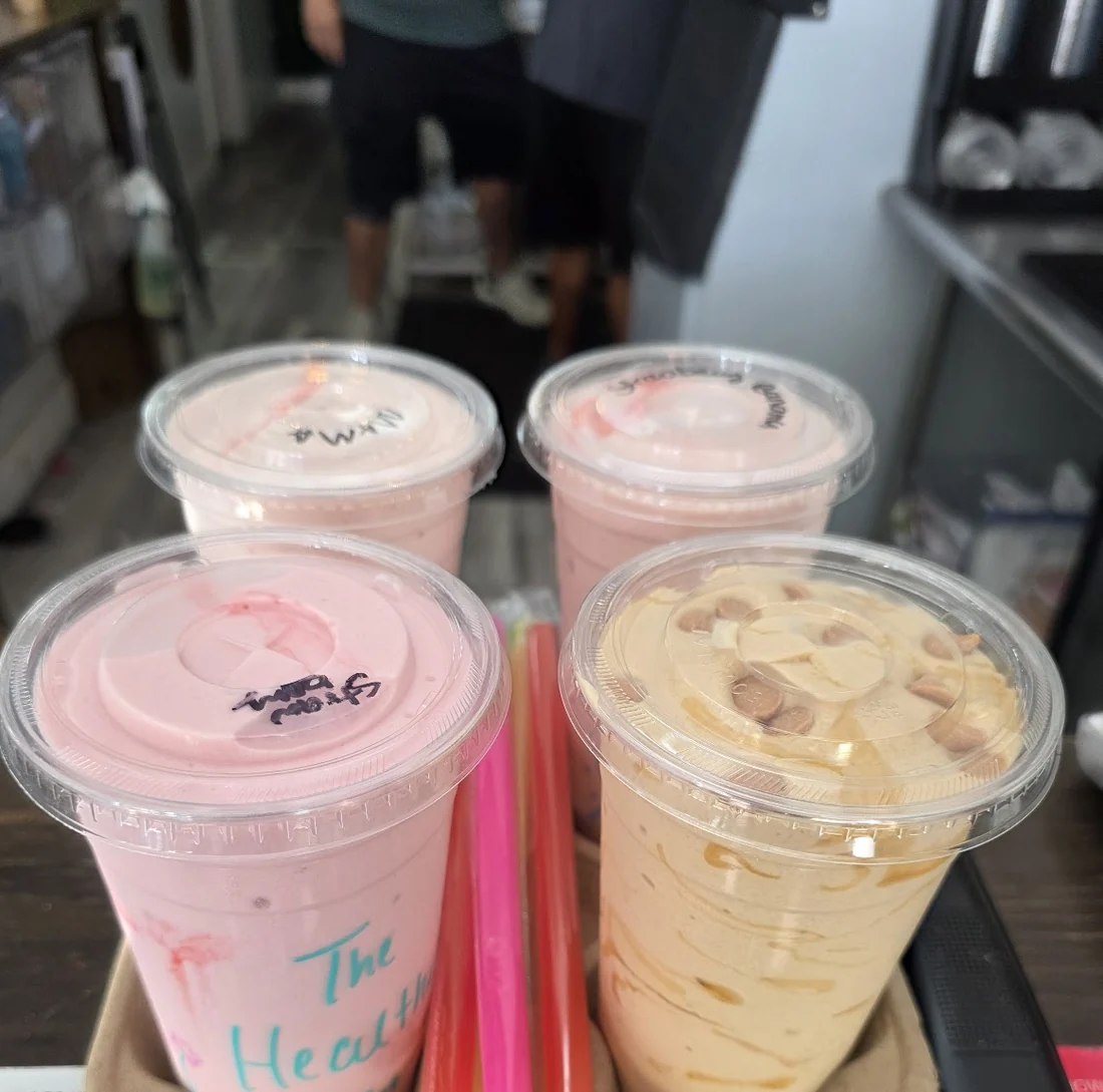 Bandeja con cuatro batidos rosados y anaranjados, cada vaso rotulado a mano con un nombre