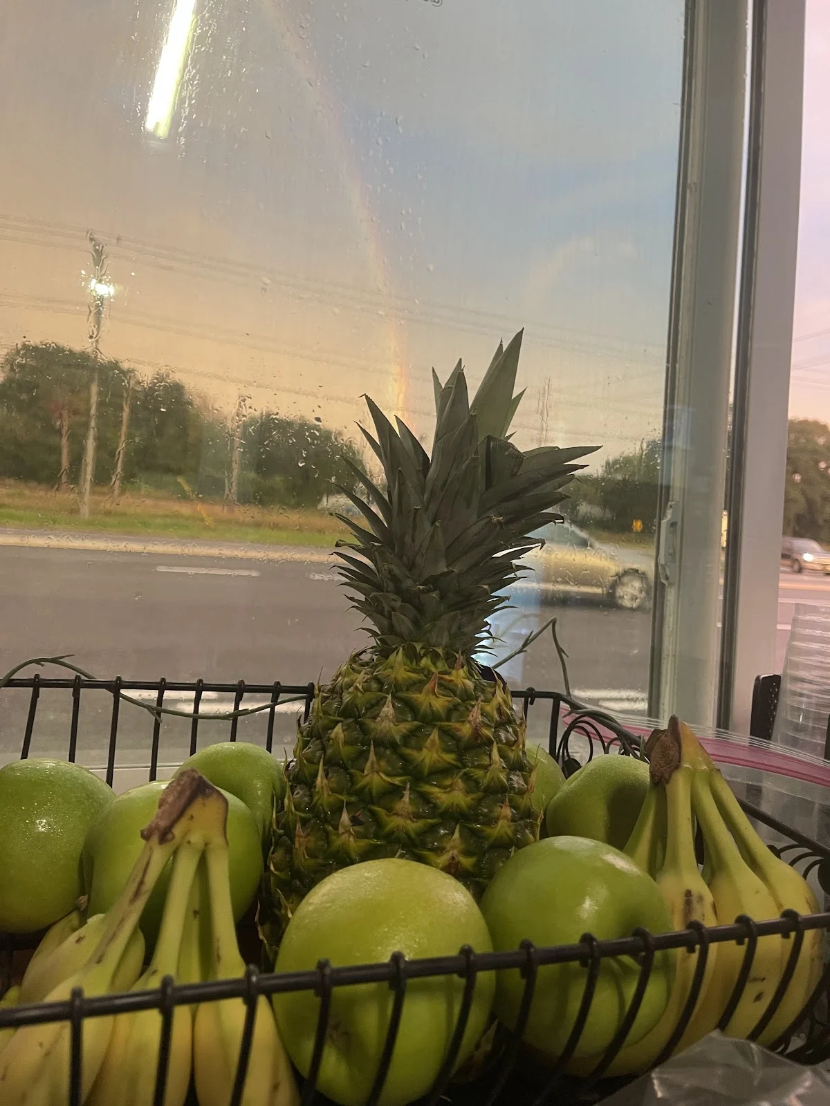 Canasta con piña, guineos y manzanas verdes junto a la ventana de la parada, con US-41 afuera